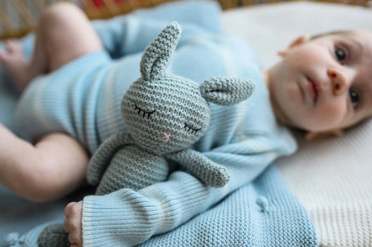 Baby in soft blue knitwear holding a knitted bunny toy on a cozy blanket