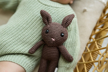 Brown knitted bunny toy resting on baby in green knitwear