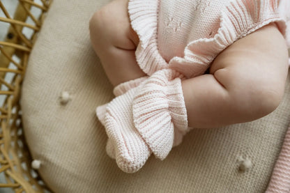Baby wearing light pink knitwear outfit sitting on a textured beige cushion